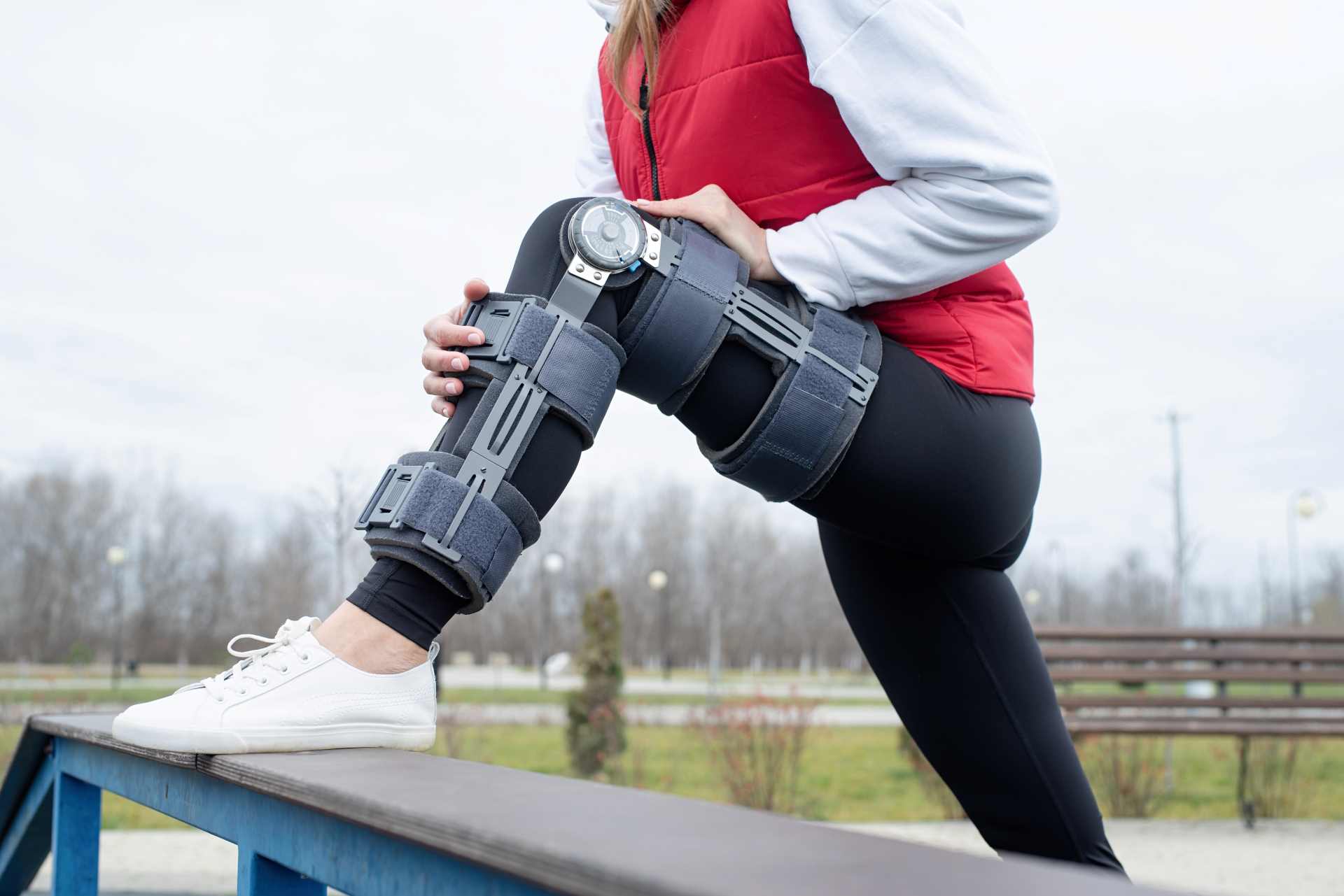 Woman stretching leg with knee brace on | Featured image for Recovering from Knee Injury blog for Refine Health Group.