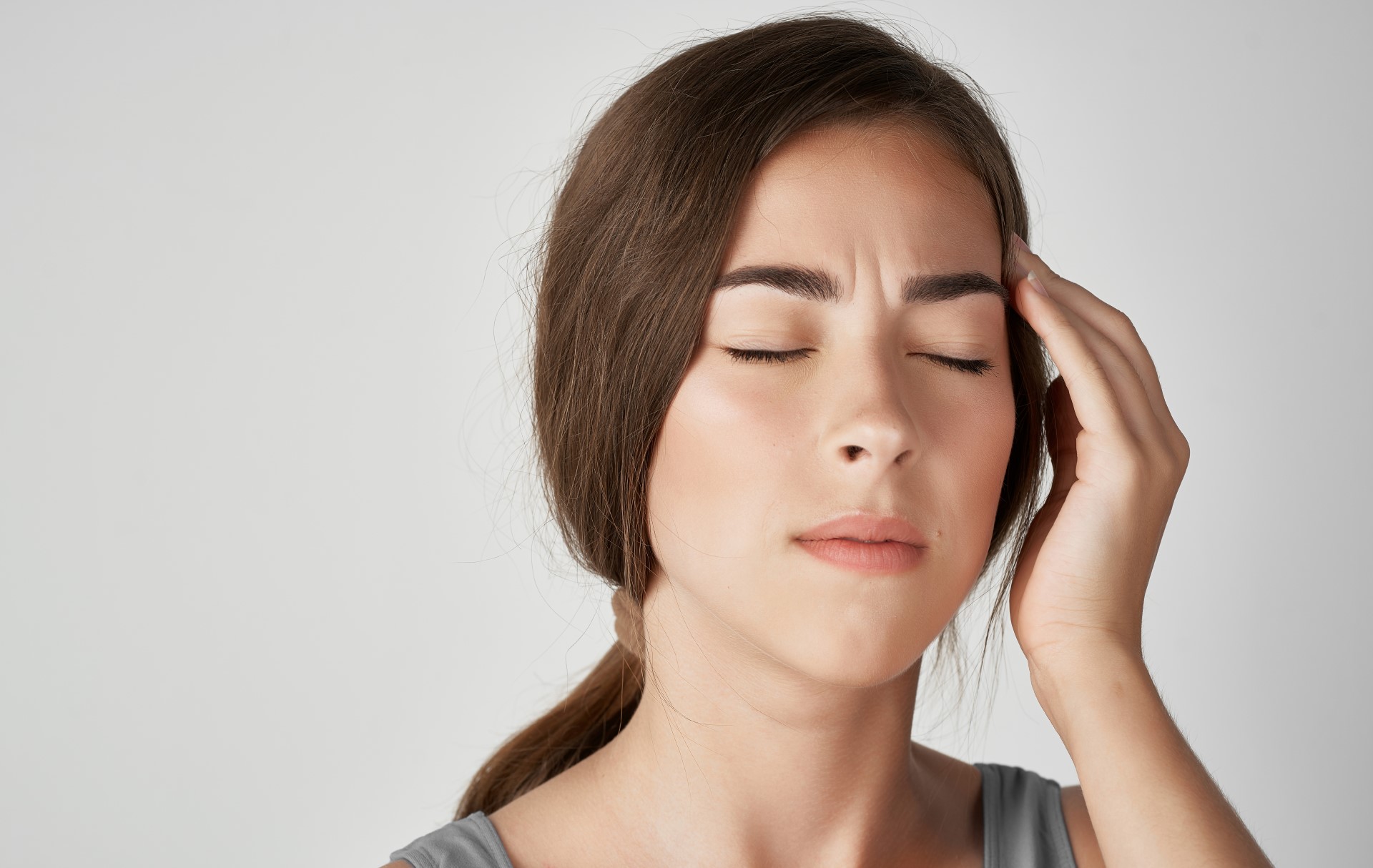 A woman with a headache | Featured image for The Different Kinds of Headaches and Migraines blog from Refine Health Group.